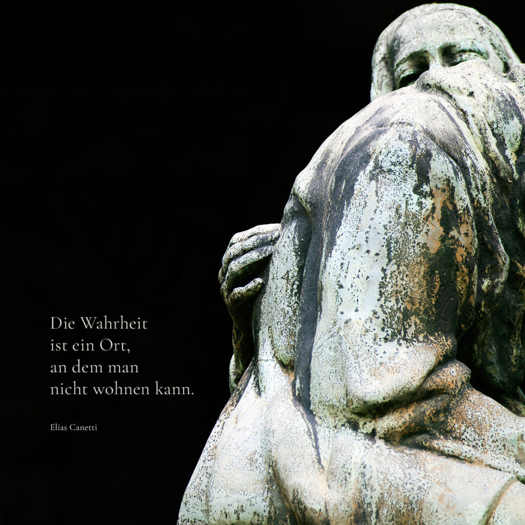 Eine verwitterte Steinskulptur eines Paares tritt aus dunklem Hintergrund hervor. Links steht in weißer Schrift das Zitat: "Die Wahrheit ist ein Ort, an dem man nicht wohnen kann." - Conetti. Kontemplative Fotografie aus dem Projekt "Zwischen Tau und Wind" von Katrin Jeschke